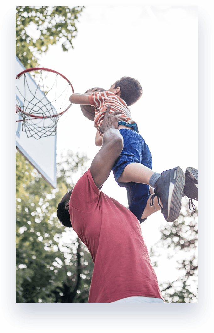 man lifting kid with basketball to basketball hoop